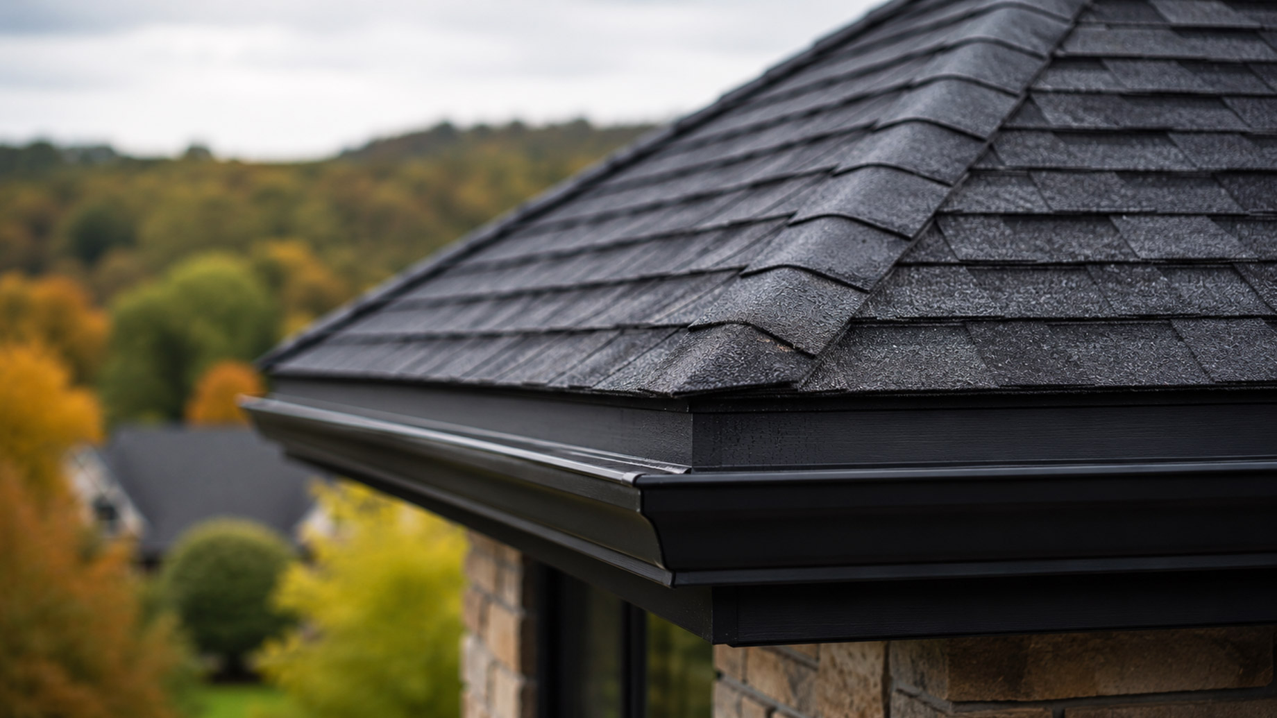Close-up of a Smithton, Pennsylvania property roof with dark architectural shingles, clean black gutters, stone exterior details, and autumn trees in the background.