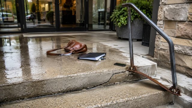 Wet concrete entrance with a damaged handrail and scattered personal belongings after a property-related fall.
