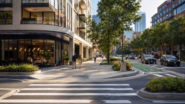 Tree-lined New York City street with luxury residences, wide sidewalks, protected cycling lanes, crosswalks, and active storefronts.