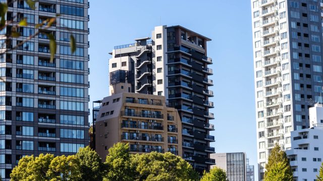Contemporary apartment towers rise above green trees in a central Tokyo residential district under a clear blue sky.