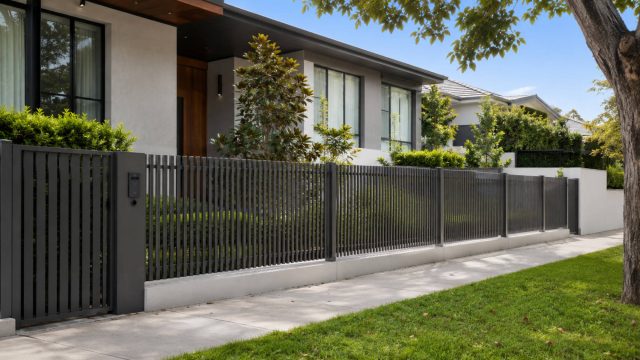 Dark powder-coated aluminium fence with vertical slats in front of a contemporary home with landscaped greenery.