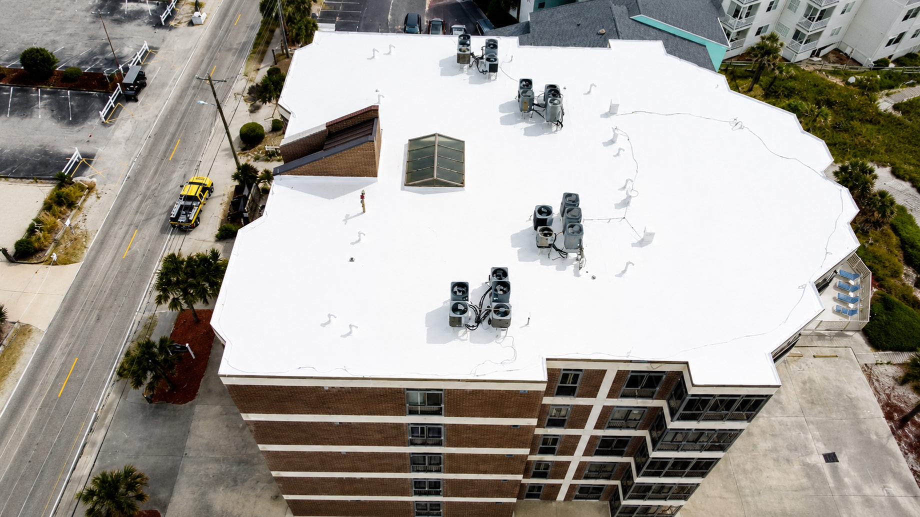 Aerial view of a large white commercial flat roof with multiple HVAC units near a coastal Myrtle Beach neighbourhood.