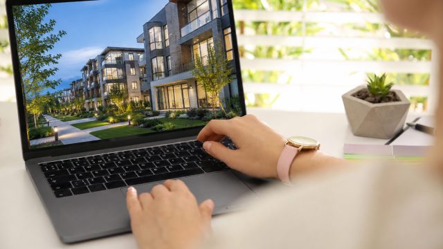 Real estate marketer reviewing a modern residential development on a laptop in a bright workspace.