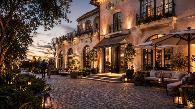 Design-led boutique hotel with illuminated architecture, landscaped courtyard seating, and guests approaching the entrance at twilight.