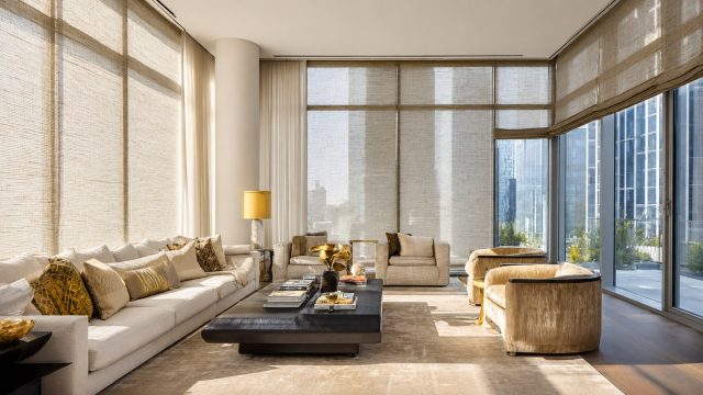 Modern living room with floor-to-ceiling windows, woven custom shades, cream seating, city views, and warm natural light.