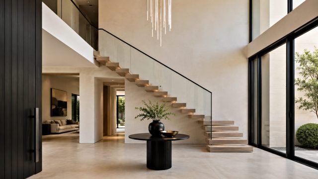 Modern luxury foyer with a floating staircase, glass railing, protected furnishings, and floor coverings prepared for a residential move.