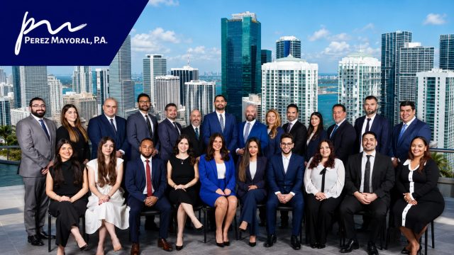Perez Mayoral, P.A. legal team posed in front of the Miami skyline with the firm’s logo displayed in the upper-left corner.