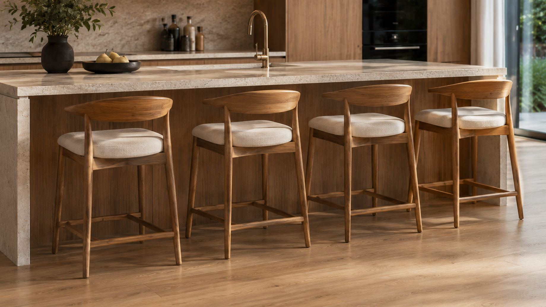 Four timber bar stools with curved backrests and upholstered seats arranged along a stone kitchen island in a warm modern interior.