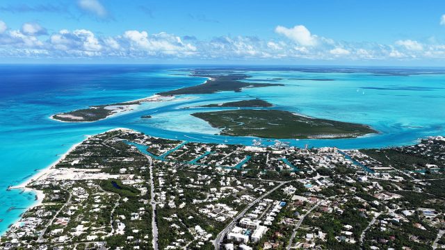 Aerial view of Providenciales with coastal neighbourhoods, canals, marinas, beaches, and turquoise waters across the Turks and Caicos Islands.