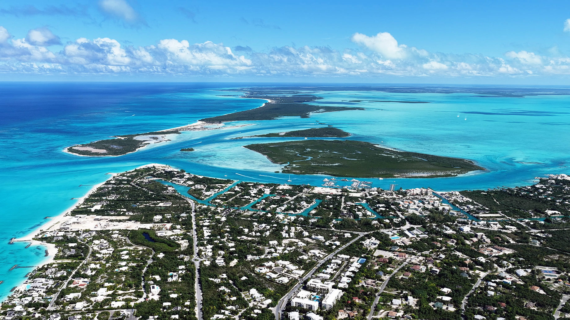 Aerial view of Providenciales with coastal neighbourhoods, canals, marinas, beaches, and turquoise waters across the Turks and Caicos Islands.