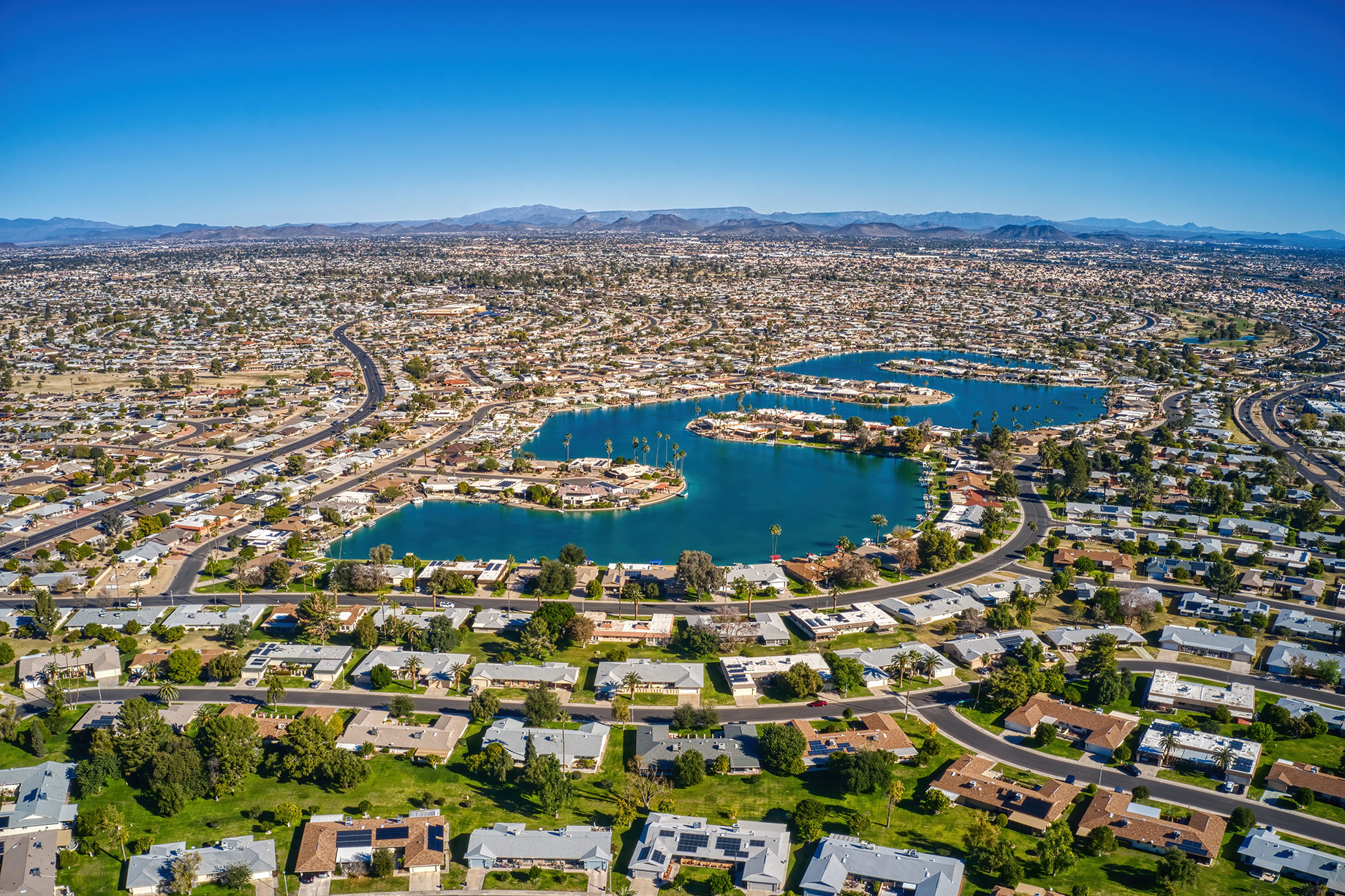 Aerial view of Sun City, Arizona, showing suburban neighborhoods, lakes, roads, and desert mountains across the Phoenix metropolitan area.