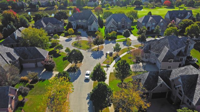 Aerial view of an upscale Chicago residential neighborhood with large homes, landscaped lawns, mature trees, and a circular suburban street.