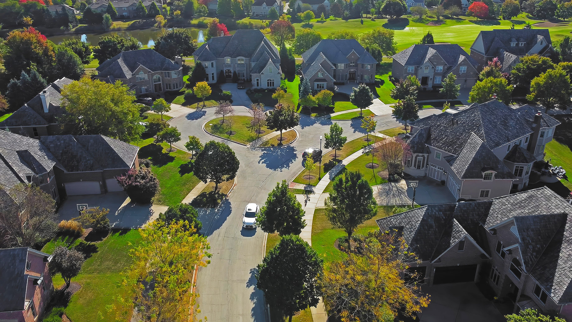 Aerial view of an upscale Chicago residential neighborhood with large homes, landscaped lawns, mature trees, and a circular suburban street.