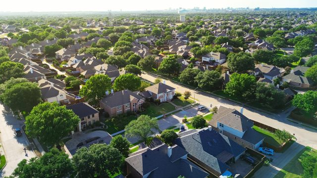 Aerial view of tree-lined suburban homes in West Plano, Texas, with a water tower and the distant Dallas skyline.