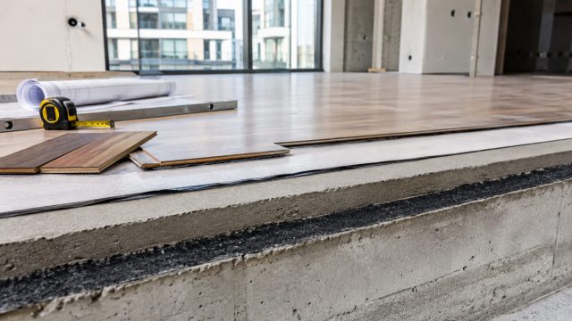 Exposed apartment floor build-up showing concrete slab, acoustic underlay, levelling layer, and timber flooring during construction.