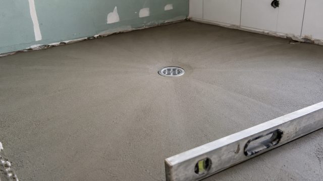 Fresh floor screed sloping toward a central drain in an Australian bathroom renovation, with a spirit level positioned across the wet-area floor.