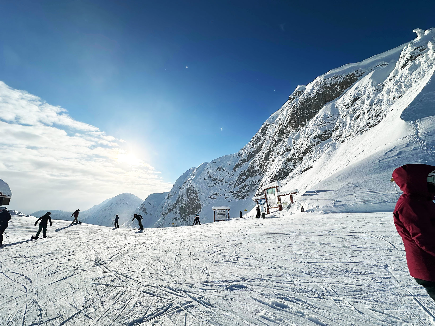 Skiers crossing a sunlit slope beneath steep snow-covered peaks at Fernie Alpine Resort.