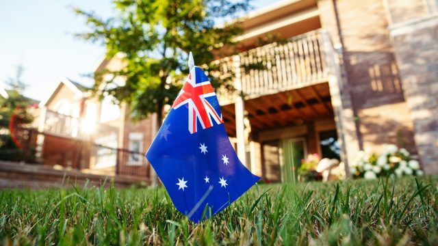 Australian flag planted in a front lawn with a residential home in the background.