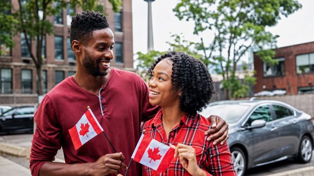 Smiling couple holding Canadian flags outdoors, representing common-law and marriage sponsorship pathways in Canada.