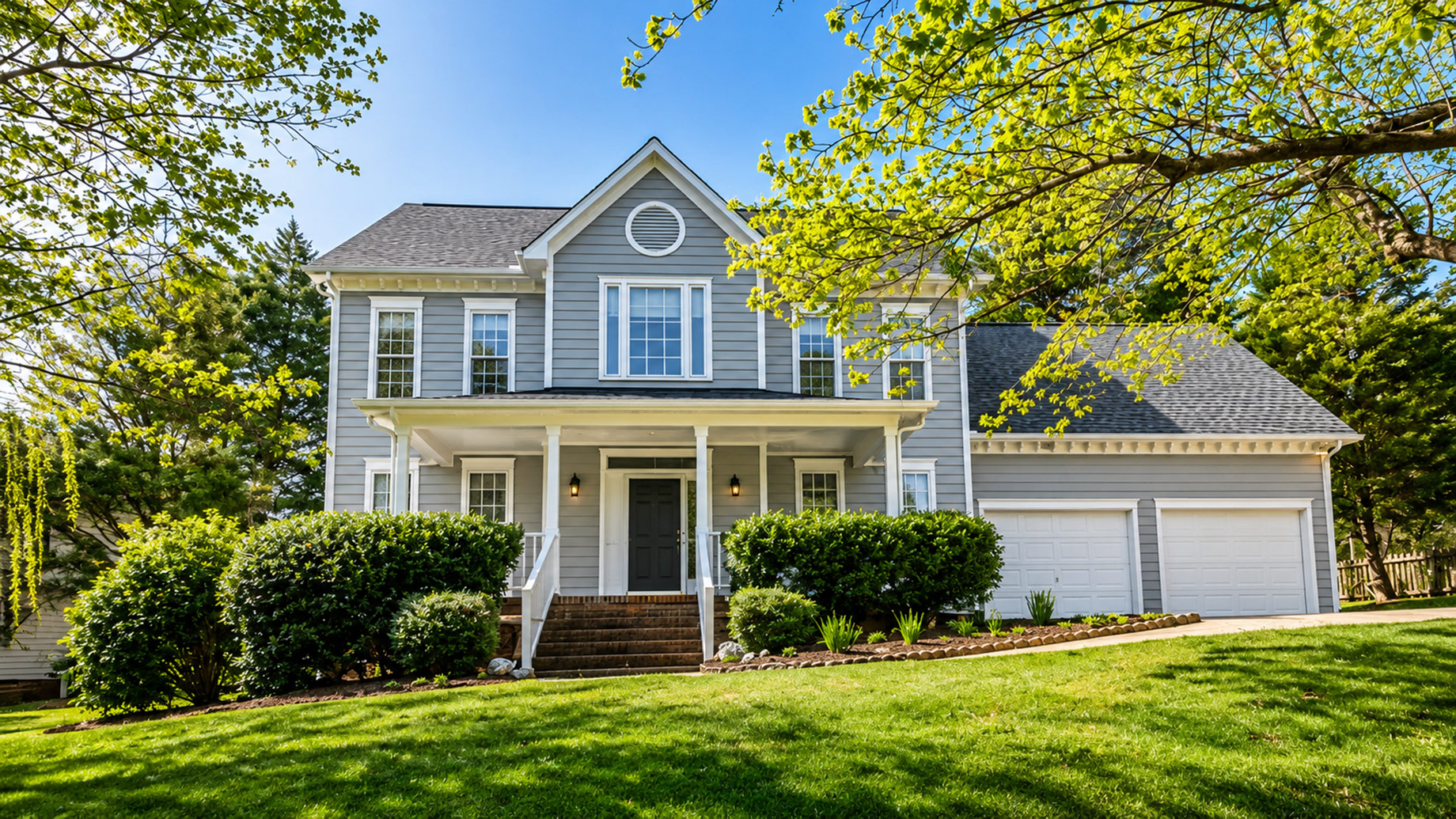Two-story suburban rental property with grey siding, an attached garage, mature trees, and a landscaped front yard.
