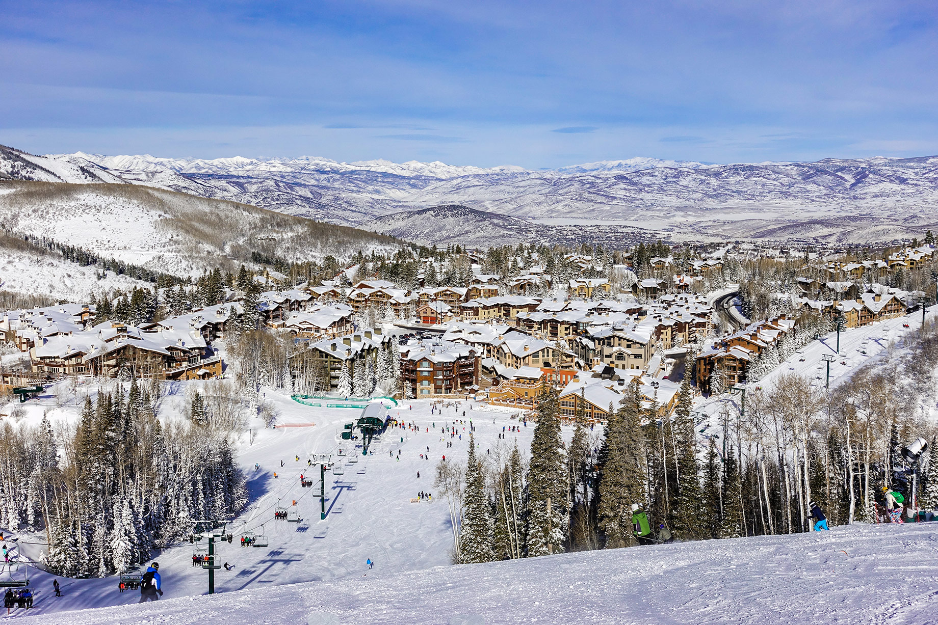 Chairlifts and skiers descending snowy slopes toward Deer Valley resort buildings near Park City, Utah.