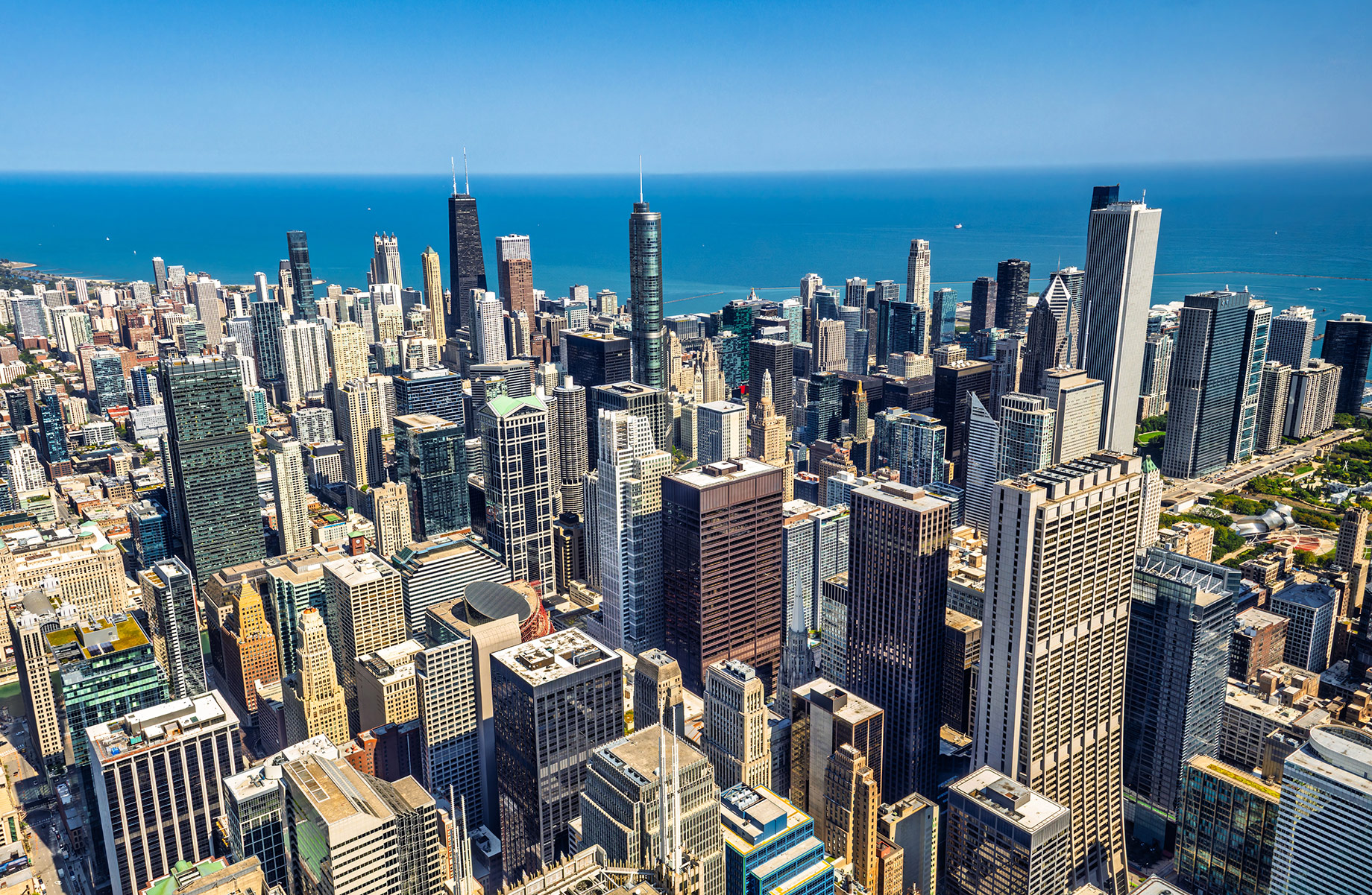 Aerial view of downtown Chicago skyscrapers beside Lake Michigan under a clear blue sky.