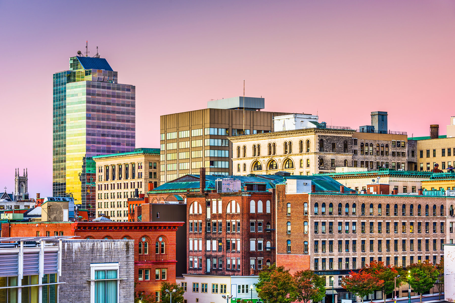 Downtown Worcester, Massachusetts skyline with historic brick buildings and modern high-rises beneath a colorful evening sky.
