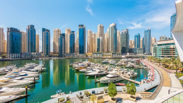 Luxury yachts moored in Dubai Marina with modern residential skyscrapers rising along the waterfront under a clear blue sky.