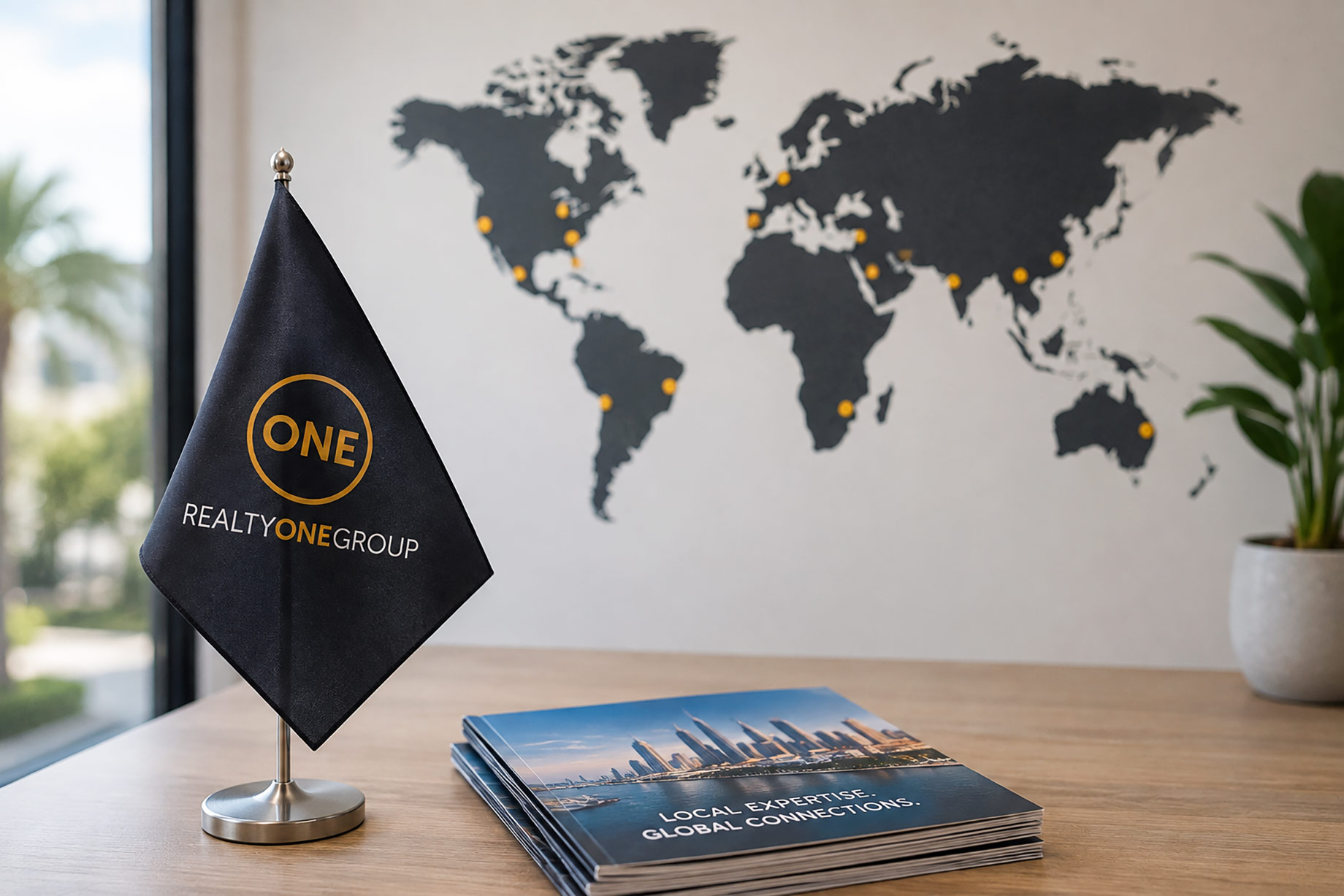 Realty ONE Group desk flag beside global real estate materials with a world map and international market locations in the background.
