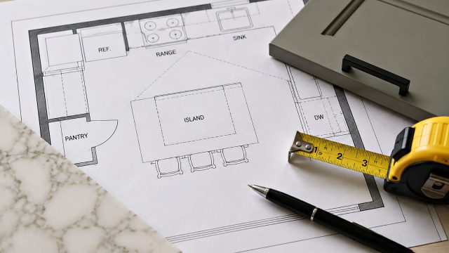 Kitchen floor plan with cabinet sample, countertop material, tape measure, and pen arranged for renovation planning.