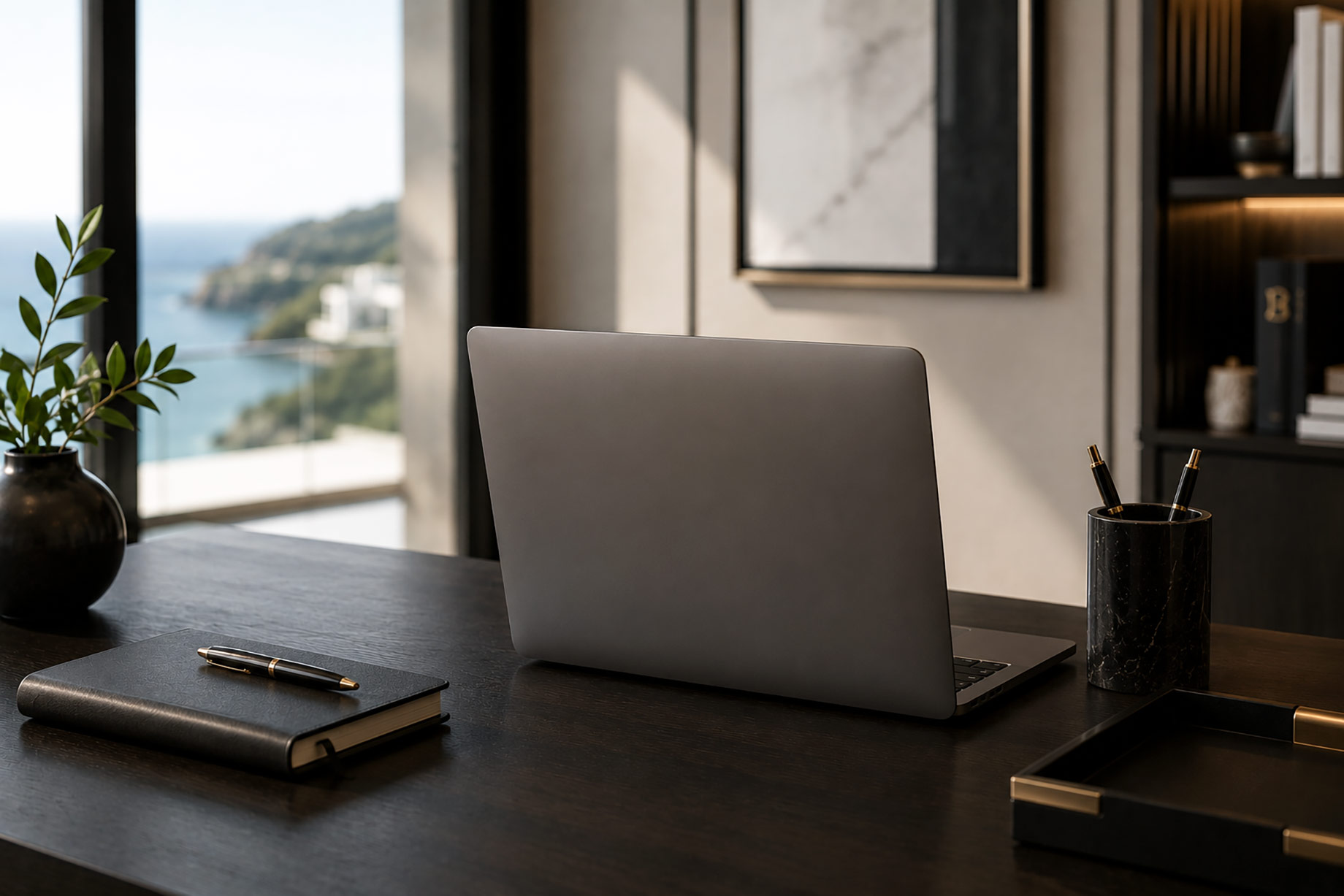 Laptop on a refined executive desk with a notebook, pens, and coastal views in a minimalist luxury office.