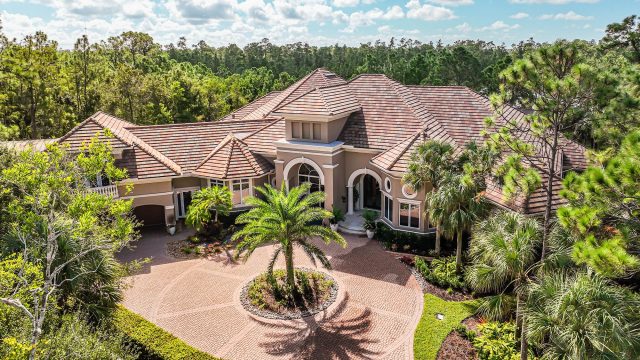 Luxury estate in Naples, Florida, with a circular paver driveway, palm trees, tropical landscaping, and Mediterranean-inspired architecture.