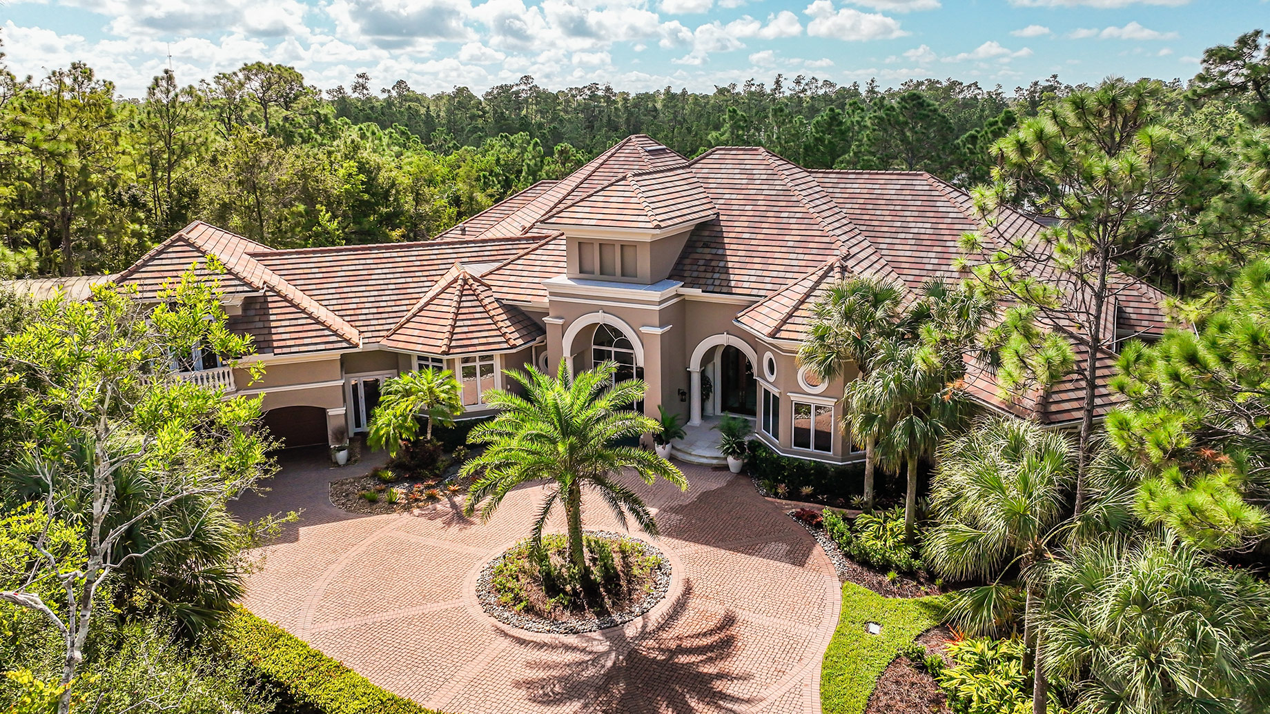Luxury estate in Naples, Florida, with a circular paver driveway, palm trees, tropical landscaping, and Mediterranean-inspired architecture.