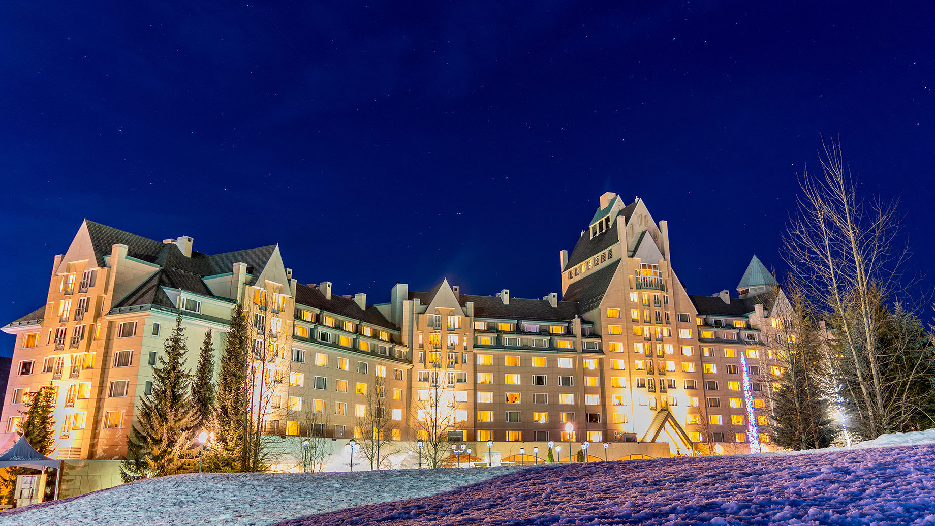Illuminated luxury hotel at the base of Whistler Mountain beneath a clear, star-filled winter sky.