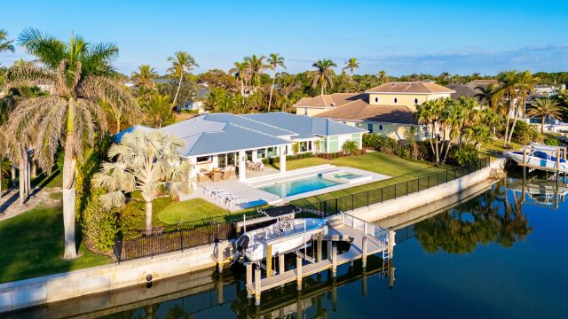 Luxury waterfront home in Naples, Florida, with a manicured natural lawn, swimming pool, palm trees, private dock, and boat along a canal.
