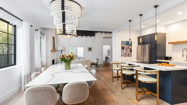 Modern open-plan luxury kitchen with deep blue cabinetry, white marble countertops, stainless steel appliances, pendant lighting, and gold-accented seating.