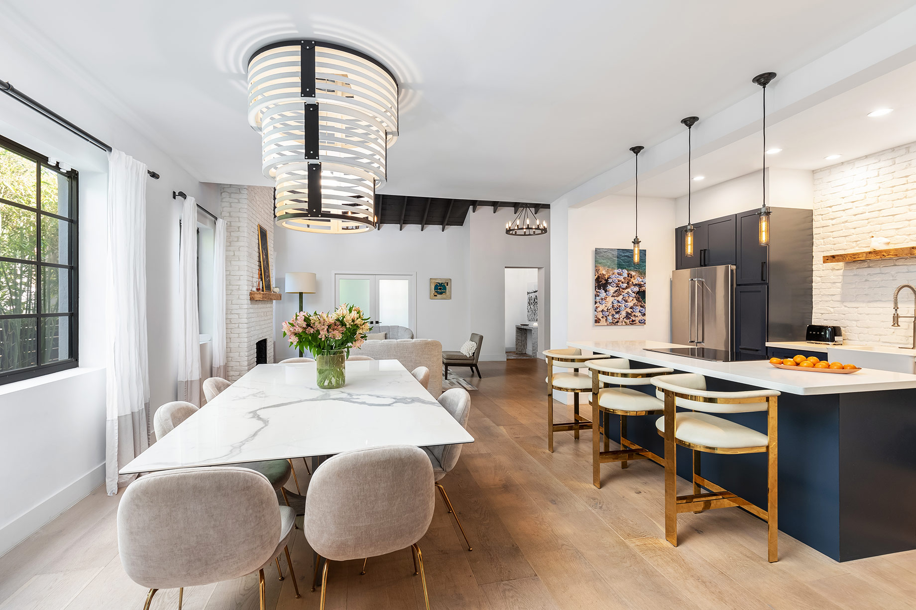 Modern open-plan luxury kitchen with deep blue cabinetry, white marble countertops, stainless steel appliances, pendant lighting, and gold-accented seating.