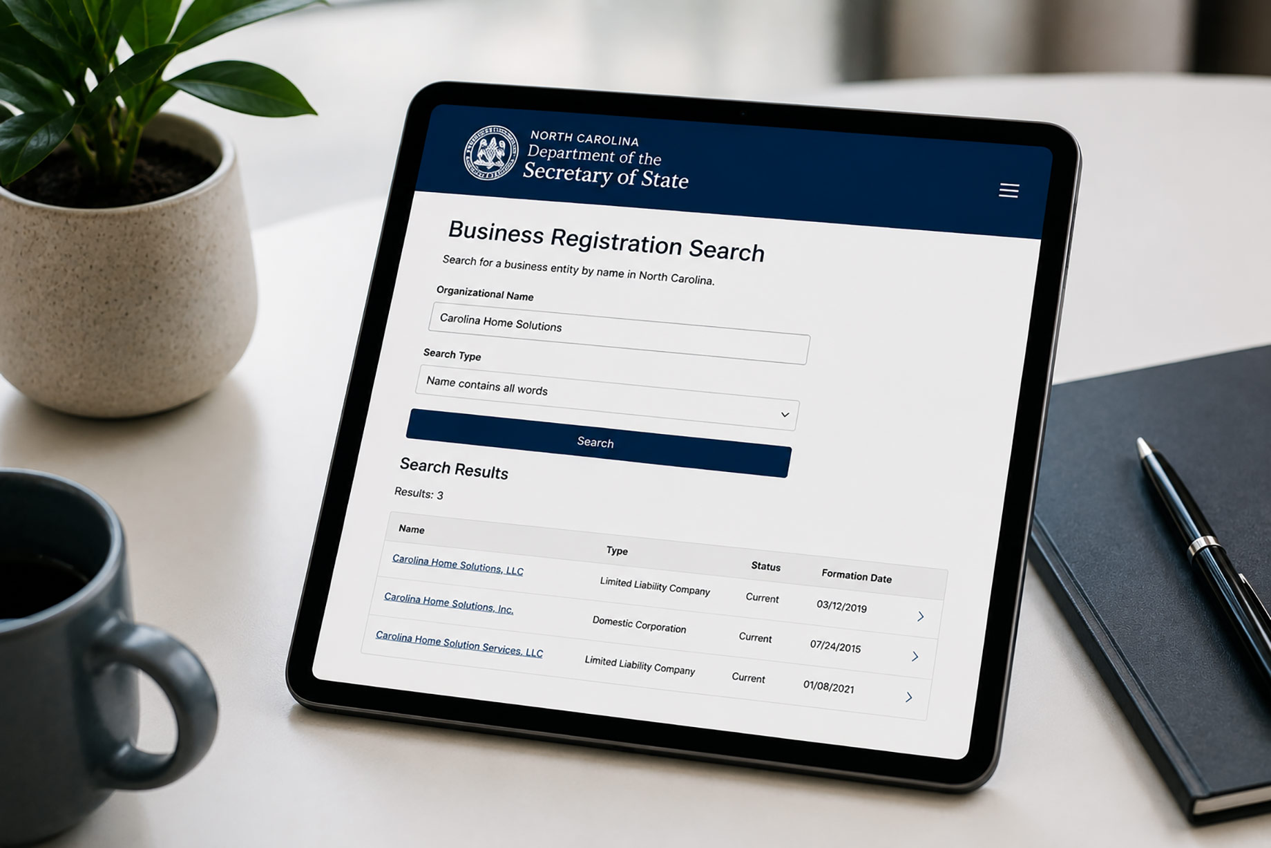 iPad displaying the North Carolina Secretary of State Business Registration Search beside a coffee mug, notebook, and potted plant.