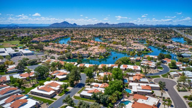 Aerial view of a North Scottsdale neighborhood with residential homes, community lakes, palm trees, and desert mountains under a clear blue sky.