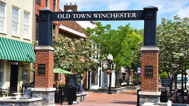 Old Town Winchester entrance arch overlooking the historic pedestrian district with brick buildings, local shops, mature trees, and landscaped public spaces.
