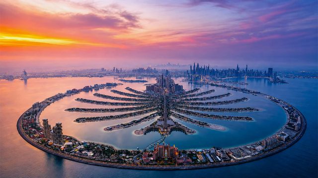 Aerial view of Palm Jumeirah at sunset with Dubai’s waterfront skyline extending across the horizon.