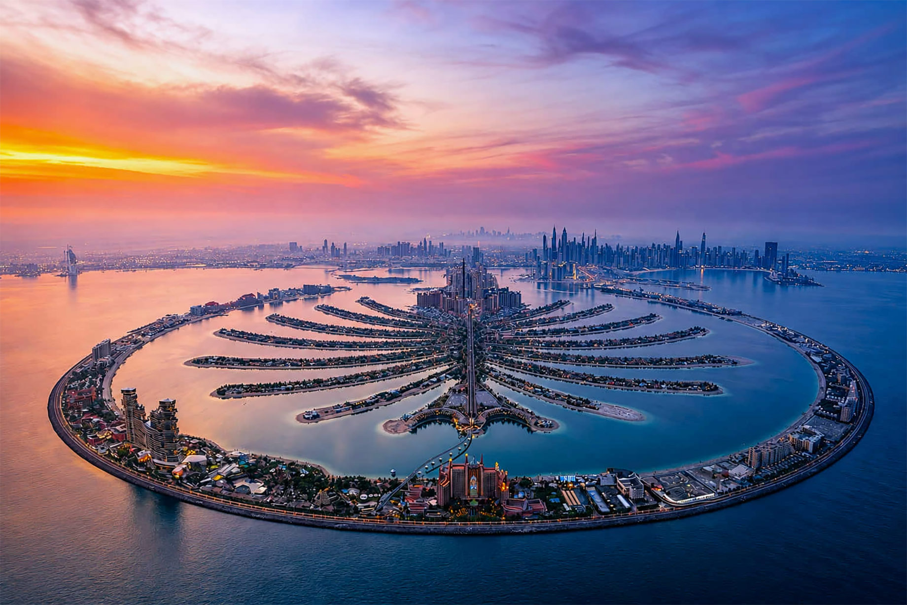 Aerial view of Palm Jumeirah at sunset with Dubai’s waterfront skyline extending across the horizon.