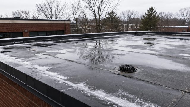 Standing water and partially frozen areas surrounding a roof drain on a flat commercial building during the winter season.