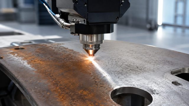 Pulse laser cleaning head removing rust from a metal plate in an industrial manufacturing environment.
