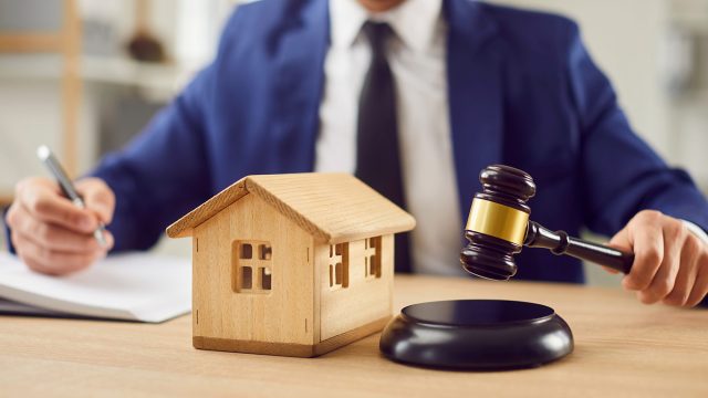 Real estate lawyer with a judge’s gavel and wooden house model representing a property ownership or title dispute.