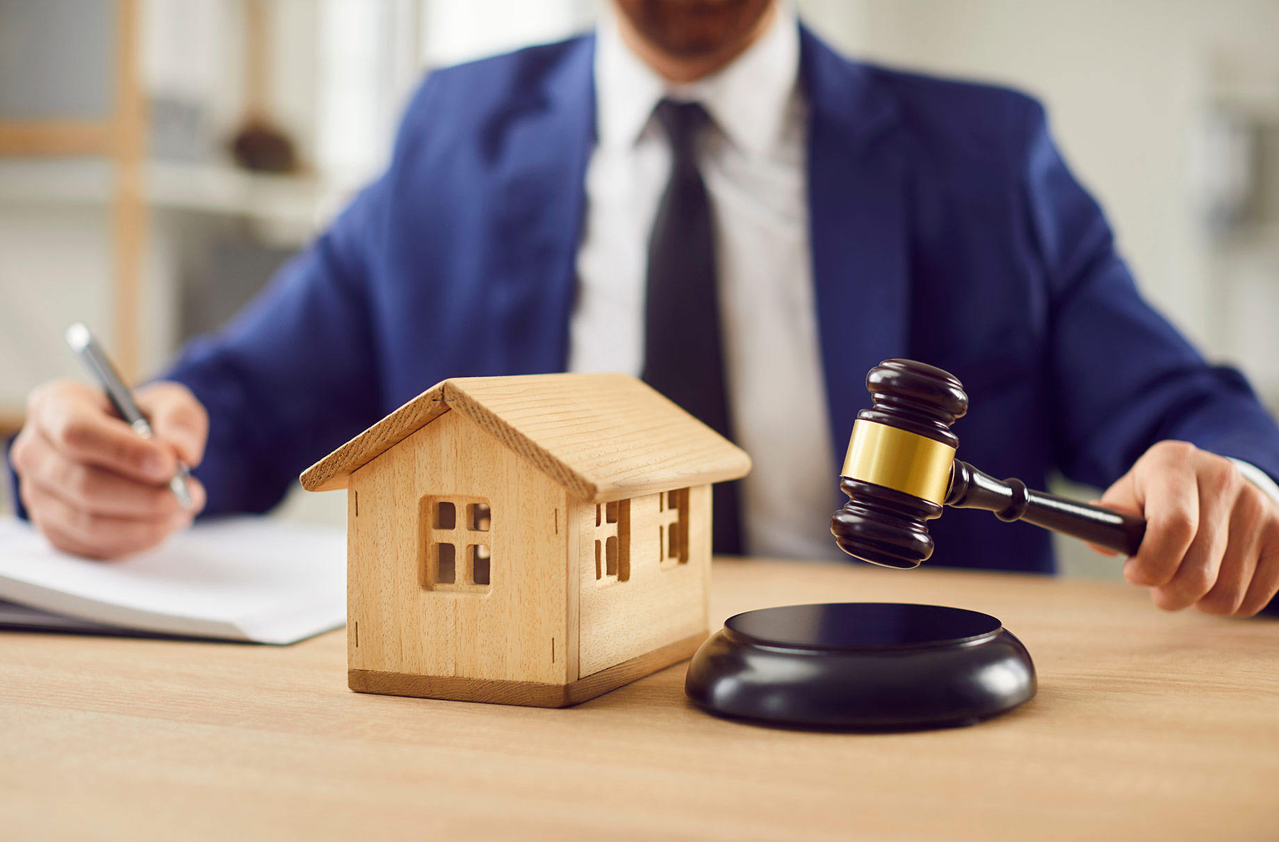 Real estate lawyer with a judge’s gavel and wooden house model representing a property ownership or title dispute.