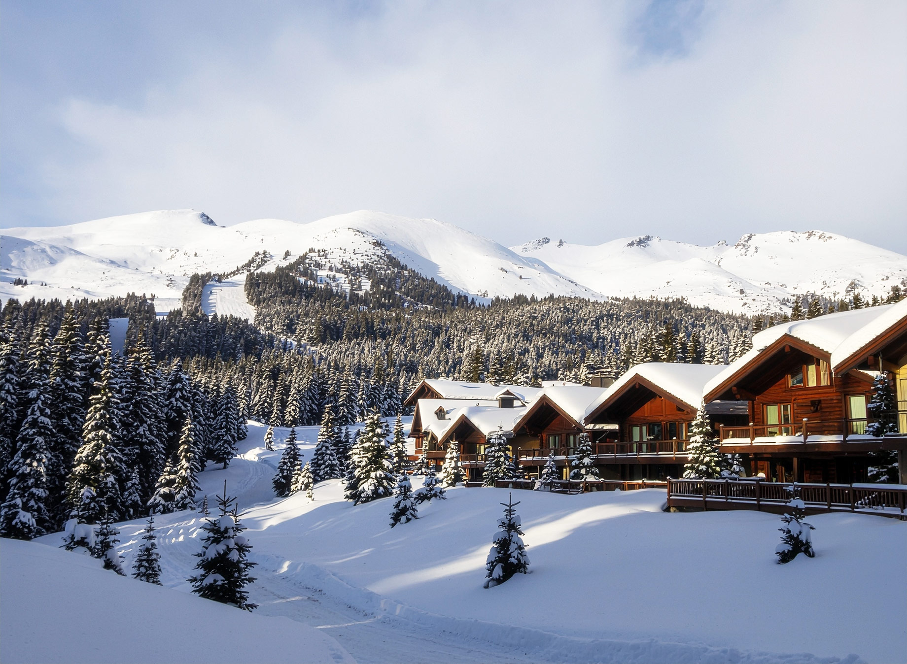 Wooden ski chalets surrounded by deep snow and evergreen forest beneath the mountains near Whistler.