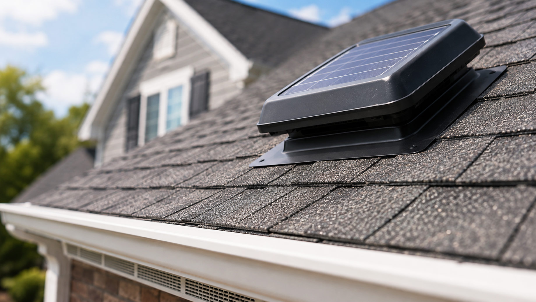 Close-up of a solar-powered attic ventilation fan installed on asphalt roof shingles with soffit ventilation visible below.