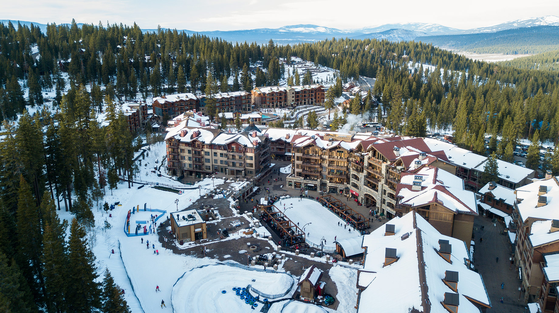 Aerial view of Northstar California resort buildings, snowy forests, and Lake Tahoe in the distance