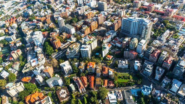 Aerial view of a dense urban residential area with apartment buildings, houses, tree-lined streets, and mixed property types.